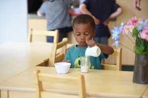 Child sits at a table and pours milk into a cup